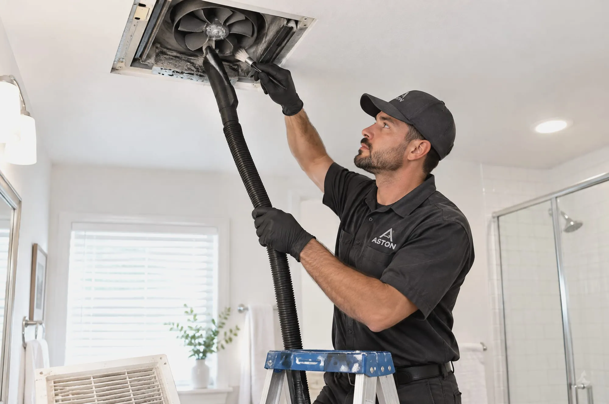 Technician cleaning a bathroom ceiling exhaust fan
